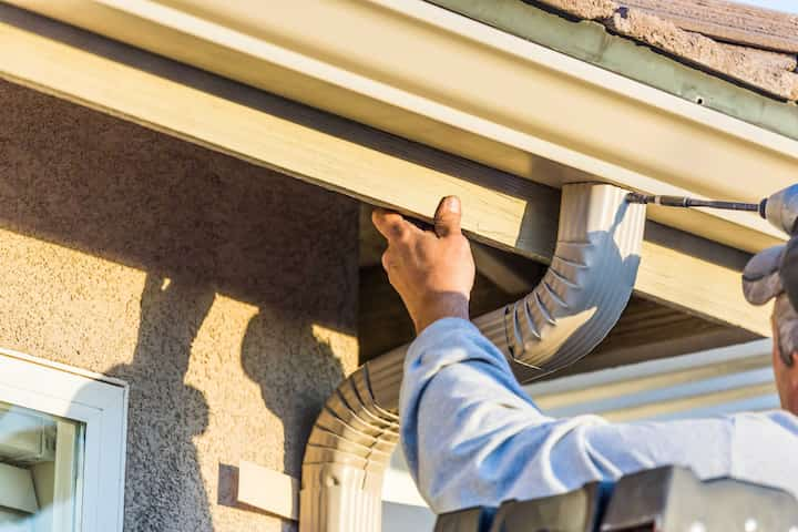 A gutter installation expert secures a gutter with a drill.